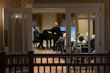 View through glass doors of a man singing opera in front of a piano