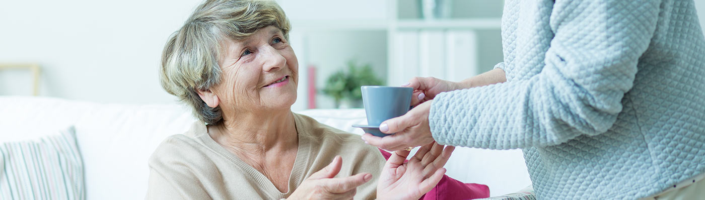 senior taking cup of tea from caregiver