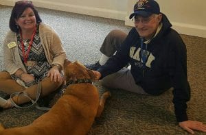 Resident Jack K. with a therapy dog and woman sitting on the floor