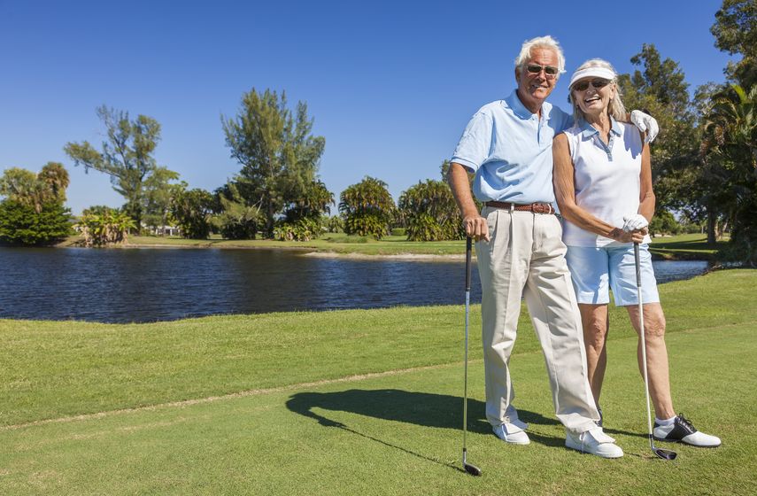 happy senior man and woman couple together playing golf on a course near a lake